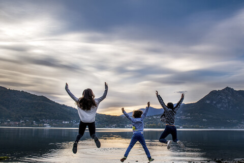 Rear view of boy and young women jumping mid air by river at dusk, Vercurago, Lombardy, Italy stock photo