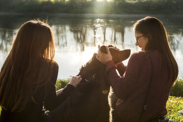 Zwei junge Frauen streicheln einen Hund am Flussufer, Calolziocorte, Lombardei, Italien - CUF01872