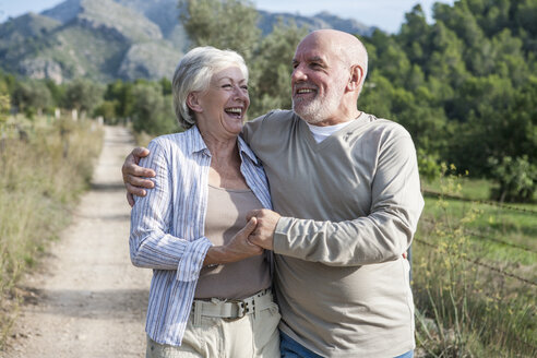 Senior couple walking together in rural setting, holding hands, smiling - CUF01884