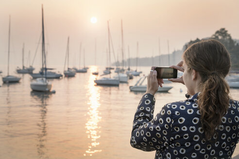 Rear view of woman photographing boats at sunset, Lazise, Veneto, Italy, Europe - CUF01888