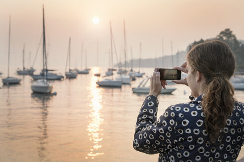 Rückansicht einer Frau, die Boote bei Sonnenuntergang fotografiert, Lazise, Venetien, Italien, Europa - CUF01888