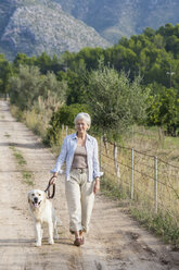 Porträt einer älteren Frau, die mit ihrem Hund spazieren geht - CUF01900