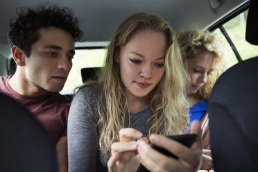 Freunde auf dem Rücksitz eines Autos schauen auf ihr Smartphone - CUF01931