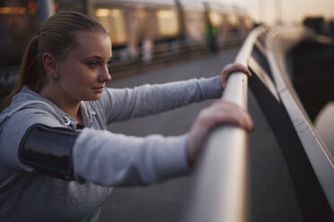 Kurvenreiche junge Frau, die in der Abenddämmerung am Geländer einer Fußgängerbrücke lehnt - CUF01944