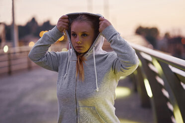 Kurvenreiche junge Frau beim Training, Kapuzenpulli auf einer Fußgängerbrücke in der Abenddämmerung - CUF01945