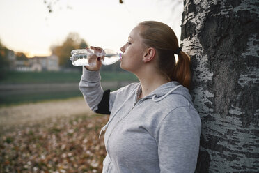 Kurvenreiche junge Frau, die im Park trainiert und Wasser in Flaschen trinkt - CUF01948