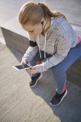 Curvaceous young woman training, sitting on wall looking at smartphone - CUF01957