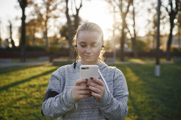 Junge Frau trainiert im Park und schaut auf ihr Smartphone - CUF01958