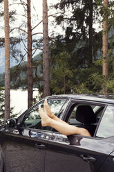Frau, die ihre Beine aus dem Autofenster streckt - CUF01974