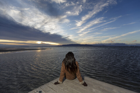 Junge Frau schaut bei Sonnenuntergang vom Pier aus, Tarragona, Katalonien, Spanien, lizenzfreies Stockfoto