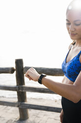 Junge Frau, die am Meer trainiert und auf ihre Smartwatch schaut - CUF02024