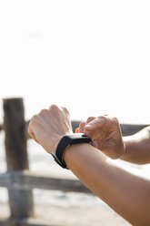 Junge Frau beim Training am Meer mit Blick auf eine Smartwatch, Nahaufnahme der Hände - CUF02025