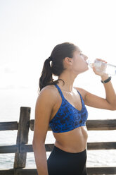 Junge Frau beim Training am Meer, trinkt Wasser in Flaschen - CUF02029