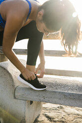 Young woman training on beach, tying trainer laces - CUF02034