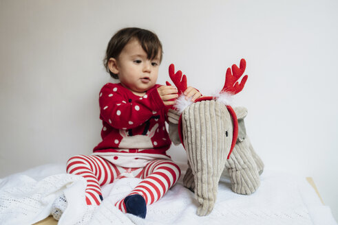 Baby girl playing with reindeer antlers headband and toy elephant - GEMF01944