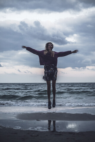 Porträt einer jungen Frau, die in der Abenddämmerung am Strand springt, Oblast Odessa, Ukraine, lizenzfreies Stockfoto