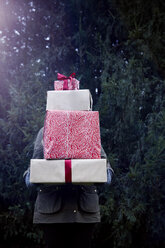 Frau trägt einen Stapel Weihnachtsgeschenke, Tannenbaum im Hintergrund - CUF02081