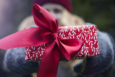 Frau hält Weihnachtsgeschenk mit roter Schleife hoch - CUF02082