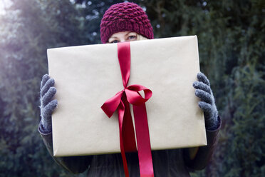 Frau hält Weihnachtsgeschenk mit roter Schleife hoch - CUF02083