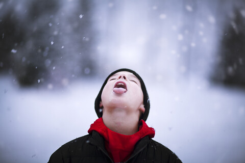 Porträt eines Jungen, der fallenden Schnee auf der Zunge auffängt, lizenzfreies Stockfoto