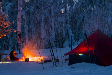 Mann sitzt am Lagerfeuer, nachts, in der Nähe des Zeltes, im schneebedeckten Wald, Russland - CUF02134