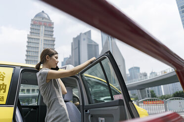 Junge Geschäftsfrau beim Aussteigen aus einem gelben Taxi im Finanzzentrum von Shanghai, Shanghai, China - CUF02185