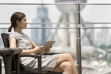 Junge Geschäftsfrau mit digitalem Tablet in einem Straßencafé im Finanzzentrum von Shanghai, Shanghai, China - CUF02188
