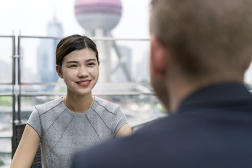 Blick über die Schulter auf eine junge Geschäftsfrau und einen Mann, die sich in einem Straßencafé im Finanzzentrum von Shanghai treffen, Shanghai, China - CUF02190