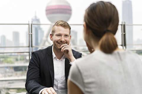 Blick über die Schulter auf einen jungen Geschäftsmann und eine Frau, die sich in einem Straßencafé im Finanzzentrum von Shanghai treffen, Shanghai, China, lizenzfreies Stockfoto