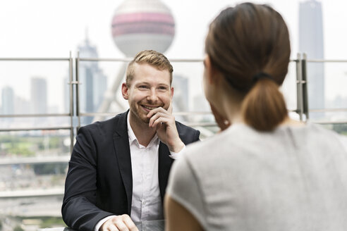 Over shoulder view of young businessman and woman having meeting at sidewalk cafe in Shanghai financial centre, Shanghai, China - CUF02191