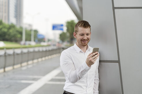 Junger Geschäftsmann mit Blick auf Smartphone-Touchscreen in der Stadt, Shanghai, China - CUF02195