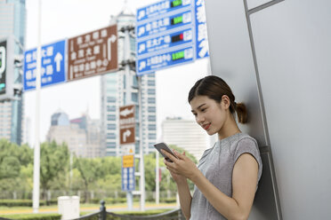 Junge Geschäftsfrau schaut in der Stadt auf ihr Smartphone, Shanghai, China - CUF02199