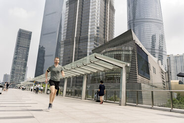 Young male runner running in Shanghai financial centre, Shanghai, China - CUF02201