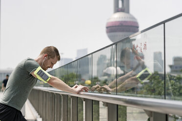 Junger männlicher Läufer lehnt an einem Geländer im Finanzzentrum von Shanghai, Shanghai, China - CUF02203