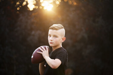 Porträt eines selbstbewussten Jungen, der American Football übt und einen Ball im Garten hält - CUF02205