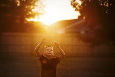 Boy practicing american football in garden reaching for a catch at sunset - CUF02206