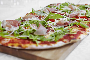 Fresh pizza with rocket and parma ham on chopping board - CUF02374