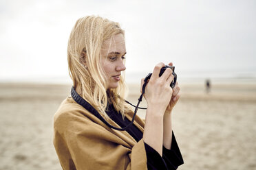 Blonde junge Frau mit Kamera am Strand - MMIF00016