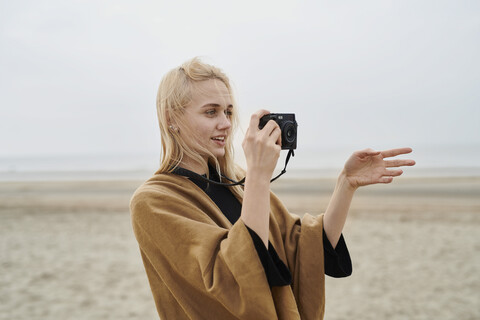 Netherlands, portrait of blond young woman with camera on the beach stock photo