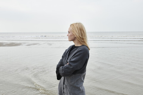 Niederlande, blonde junge Frau steht am Strand und schaut in die Ferne, lizenzfreies Stockfoto