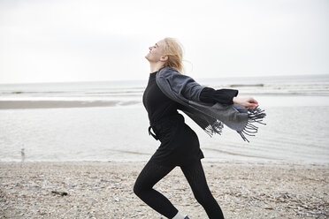 Niederlande, glückliche blonde junge Frau, die am Strand läuft - MMIF00029