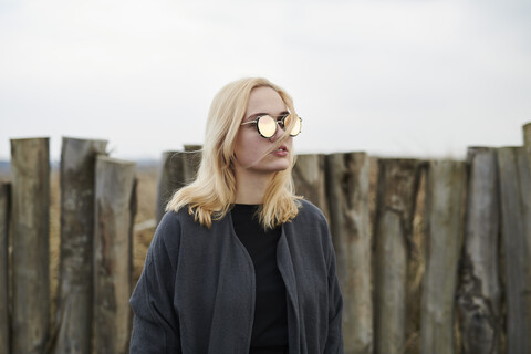 Porträt einer blonden jungen Frau mit verspiegelter Sonnenbrille am Strand, lizenzfreies Stockfoto