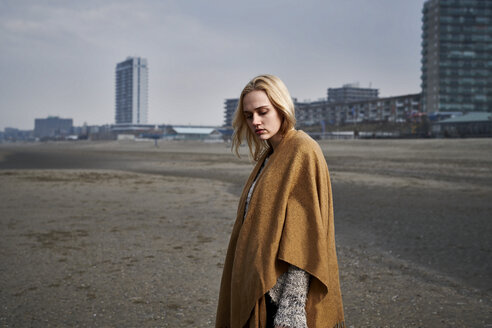 Netherlands, Zandvoort, portrait of blond young woman on the beach wearing light brown cape - MMIF00051