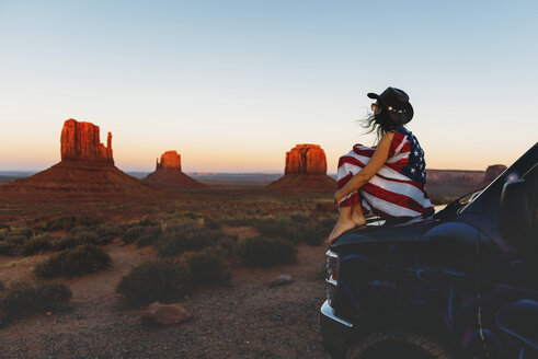 USA, Utah, Frau mit Flagge der Vereinigten Staaten von Amerika genießt den Sonnenuntergang im Monument Valley - GEMF01949