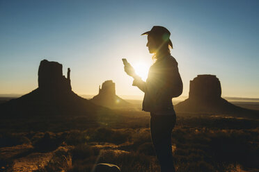 USA, Utah, Frau benutzt Handy bei Sonnenaufgang im Monument Valley - GEMF01953