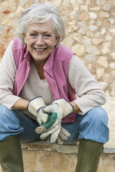 Porträt einer älteren Frau im Freien, die Gartenhandschuhe trägt - CUF02476
