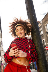 Porträt einer jungen Frau im Freien, die Kopfhörer trägt und ein Smartphone hält - CUF02508