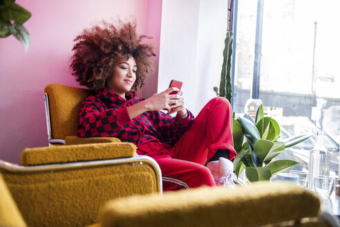 Junge Frau sitzt in einem Haus und benutzt ein Smartphone - CUF02511