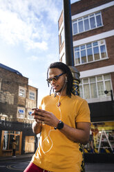 Young man outdoors, wearing earphones, using smartphone - CUF02514