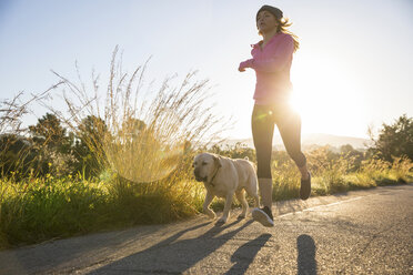 Junge Frau, die mit ihrem Hund eine Landstraße entlangläuft, Tiefblick - CUF02528